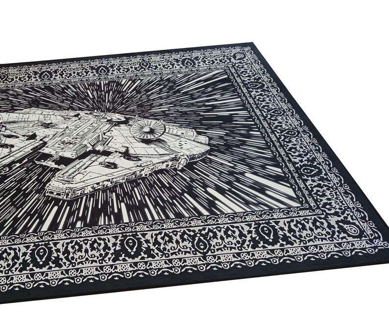 May include: Black and white Star Wars Millennium Falcon rug. The rug features a detailed illustration of the iconic spaceship against a backdrop of speed lines, with a decorative border. The rug is rectangular.