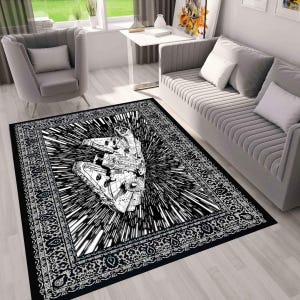 May include: Black and white area rug featuring a detailed illustration of a spaceship in a burst of speed lines. The rug has a decorative border and is placed in a living room setting.