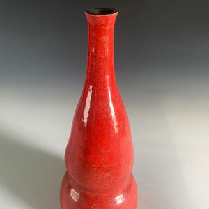 May include: A tall, red ceramic vase with a double-bulb shape. The vase has a narrow neck and a dark interior. The exterior has a crackle glaze finish, adding texture and visual interest. The vase is a decorative item.