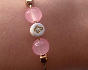 Könnte beinhalten: Ein goldenes Armband mit rosa Perlen und einer weißen Perle mit einem goldenen Kreuz.