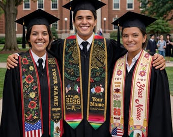 May include: Three graduates in black caps and gowns, smiling and posing outdoors. Each wears a graduation sash with text including "Your Name" and "Class of 2026". The sashes feature floral and flag designs, including the American and Mexican flags.