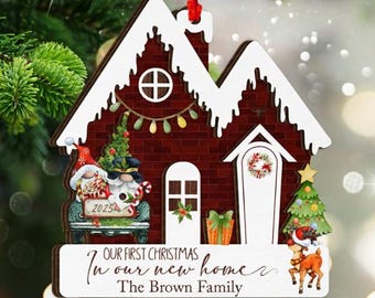 Puede incluir: Adorno navideño de madera con forma de casa, fachada de ladrillo rojo y detalles blancos. Presenta gnomos, un árbol de Navidad y el texto "Our First Christmas in our new home, The Brown Family."