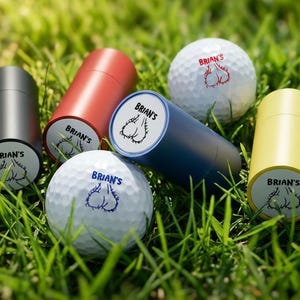 May include: Golf balls and cylindrical containers are arranged on green grass. The golf balls are white with a graphic and the name "Brian's" printed on them. The containers are in various colors, including red, blue, and yellow, and also have the name "Brian's" printed on them.