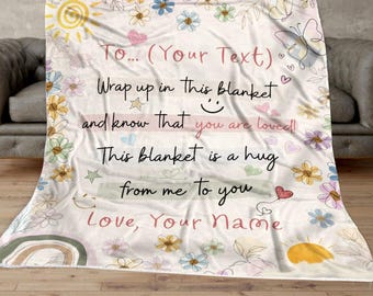 May include: A white blanket with a floral design and a message that says "To... (Your Text) Wrap up in this blanket and know that you are loved! This blanket is a hug from me to you Love, Your Name".
