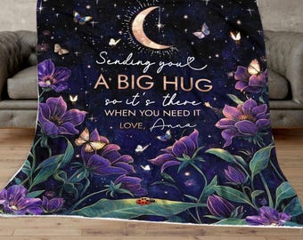 May include: A purple and green floral patterned fleece blanket with a crescent moon and stars. The text on the blanket reads "Sending you a big hug so it's there when you need it. Love, Anna."