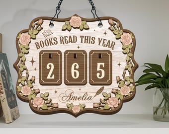 Może przedstawiać: Drewniany znak z napisem "BOOKS READ THIS YEAR" i numerem "265". Znak jest ozdobiony kwiatowymi akcentami i imieniem "Amelia". Wisi na czarnym łańcuchu.