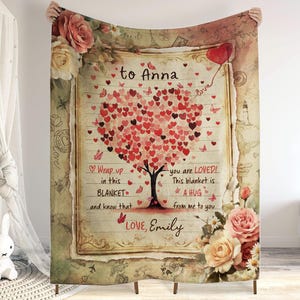 Könnte beinhalten: Eine vintage-artige Decke mit einem herzförmigen Baum aus roten Herzen. Der Text "to Anna" befindet sich oben auf der Decke, und der Text "Wrap up in this BLANKET and know that you are LOVED! This blanket is A HUG from me to you LOVE, Emily" befindet sich unten. Die Decke ist von floralen Designs umgeben.