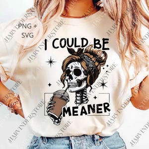 May include: Cream-colored t-shirt with a graphic of a skull with brown hair and a bandana, drinking from a coffee cup. The text reads "I COULD BE MEANER". The design includes star accents.
