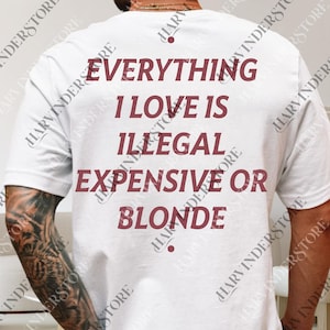 以下が含まれることがあります： 白いTシャツ。バーガンディ色の文字で「EVERYTHING I LOVE IS ILLEGAL EXPENSIVE OR BLONDE」と書かれています。クルーネックで、綿のようです。