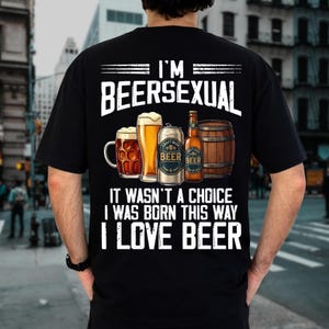 Puede incluir: Una camiseta negra con texto blanco que dice I'M BEERSEXUAL IT WASN'T A CHOICE I WAS BORN THIS WAY I LOVE BEER. El gráfico incluye una jarra de cerveza, un vaso alto, una lata plateada, una botella de vidrio marrón y un barril de madera.