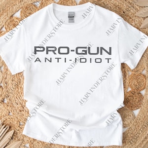 May include: White crew neck t-shirt featuring the text "PRO-GUN ANTI-IDIOT" in dark grey. The t-shirt is made of a soft material, suitable for everyday wear.