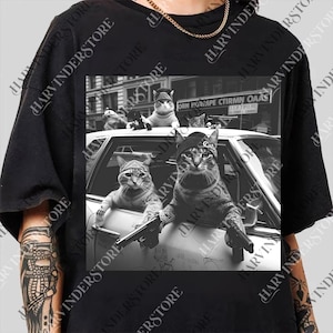 A black and white image of three cats sitting in the front seat of a car, with one of them holding a gun.