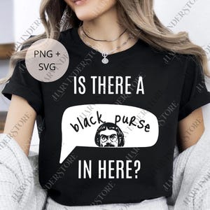 Op de afbeelding: Zwart T-shirt met witte tekst: "IS THERE A black purse IN HERE?". Een cartoonafbeelding in een tekstballon. Een casual kledingstuk voor dagelijks gebruik.