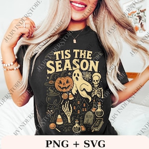 May include: Black t-shirt with a Halloween-themed graphic. The design includes a jack-o'-lantern, ghost, spiderweb, skeleton, and the text "TIS THE SEASON". Additional elements include a witch's hat, cauldron, and candy corn.