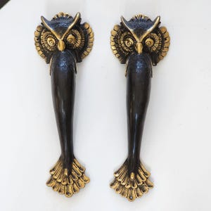 以下が含まれることがあります： フクロウのデザインが施された装飾ドアハンドルのペア。ハンドルは主に黒色で、金色がアクセントになっています。フクロウの頭とハンドルの基部は、詳細で質感のある外観をしています。ハンドルの長さは約30cmです。