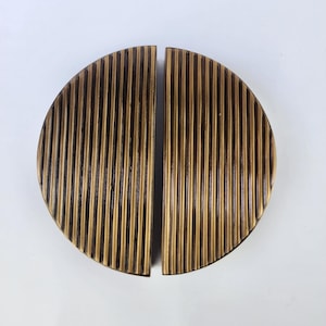 Puede incluir: Dos tiradores de armario semicirculares a juego con un diseño vertical acanalado. Los tiradores son de un color dorado antiguo cálido y están divididos por la mitad. El herraje es probablemente de metal.
