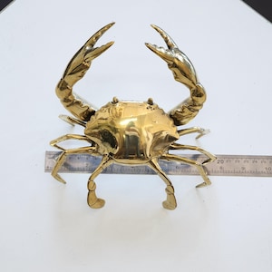 Peut inclure: Une sculpture de crabe en métal de couleur dorée. Le crabe est en position avec ses pinces levées et ses pattes tendues. La sculpture mesure environ 15 cm de large.