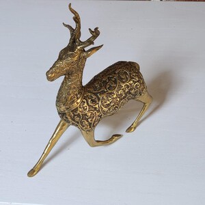 Könnte beinhalten: Eine goldfarbene Metallfigur eines Rehs mit filigranen Details. Das Reh steht auf allen vieren, der Kopf ist zur Seite gedreht. Das Reh hat einen langen Hals und einen langen Schwanz.