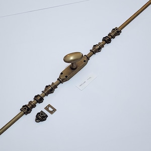 May include: A bronze window sash fastener with an oval handle and ornate detailing. Includes a matching keep and a separate decorative piece. The text "MEDIUM OVAL" is on a small white label.