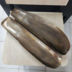 May include: Two elongated, rectangular trays with rounded corners, featuring a metallic bronze finish with a brushed, streaked texture. The trays have a shallow, concave design and a smooth, reflective surface that catches the light.