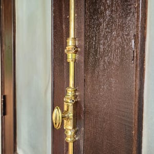 Könnte beinhalten: Ein goldfarbener Türriegel aus Metall mit einem runden Griff und einem dekorativen Design. Der Riegel ist an einer Holztür befestigt.