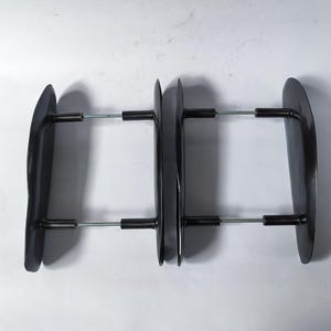 May include: Two dark bronze-toned metal door handles, each featuring a curved, elongated plate and two cylindrical mounting posts connected by thin, silver-colored threaded metal rods extending horizontally from the back of the plates.