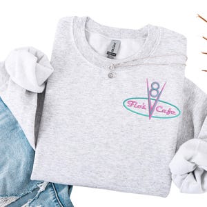 Puede incluir: Una taza de cer&aacute;mica blanca con asa negra y el texto "But First, Coffee" en negrita negra. La taza se destaca sobre un fondo borroso, resaltando su dise&ntilde;o limpio.