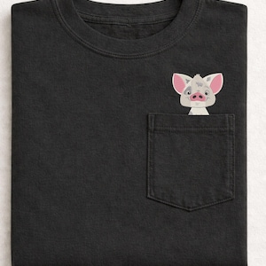 Puede incluir: Camiseta negra con un bolsillo con un cerdo de dibujos animados bordado con orejas y nariz rosas. El cerdo asoma por el bolsillo. La camiseta tiene cuello redondo y mangas cortas. La camiseta es de material suave.