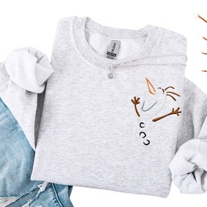 May include: A white ceramic mug with a black handle and the text "But First, Coffee" in a bold, black font. The mug is set against a blurred background. The mug is approximately 10 cm tall.