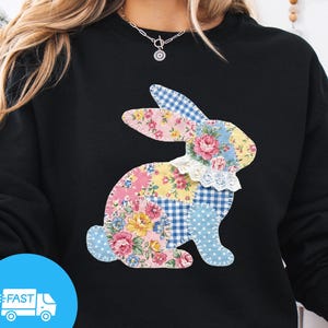 May include: Black sweatshirt featuring a patchwork bunny design with floral, gingham, and polka dot patterns. The bunny has a white lace collar. The sweatshirt has long sleeves and a crew neck. A blue circle with a white truck and the word "FAST" is in the lower left corner.
