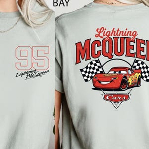 Puede incluir: Camiseta gris claro con el n&uacute;mero 95 en rojo en la parte delantera, con "Lightning McQueen" impreso debajo. La parte trasera muestra un gr&aacute;fico de Rayo McQueen con banderas a cuadros y el texto "Lightning McQueen Cars".