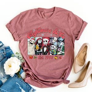 Puede incluir: Una camiseta color marr&oacute;n con un estampado gr&aacute;fico de personajes de la pel&iacute;cula "Pesadilla antes de Navidad" y el texto "Nightmare & Co. Est. 1993".