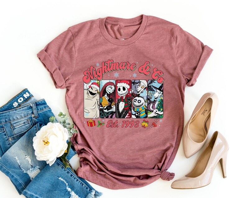 Puede incluir: Una camiseta color marr&oacute;n con un estampado gr&aacute;fico de personajes de la pel&iacute;cula "Pesadilla antes de Navidad" y el texto "Nightmare & Co. Est. 1993".