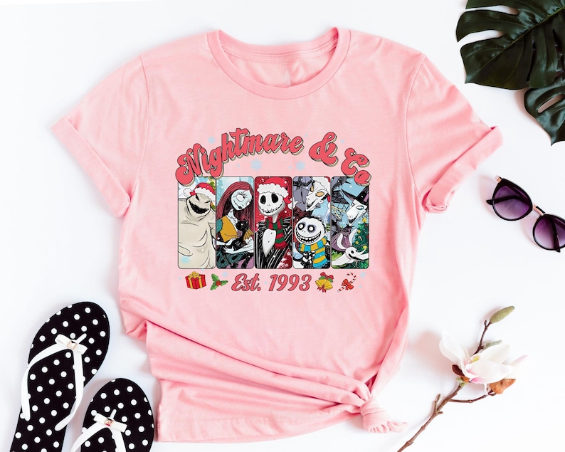 Puede incluir: Camiseta rosa con un gr&aacute;fico de personajes de la pel&iacute;cula "Pesadilla antes de Navidad" y el texto "Nightmare & Co. Est. 1993".