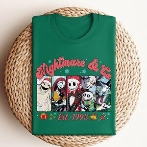 Puede incluir: Camiseta verde con un gr&aacute;fico navide&ntilde;o de personajes de la pel&iacute;cula "Pesadilla antes de Navidad". El gr&aacute;fico presenta a los personajes Jack Skellington, Sally, Oogie Boogie y Zero. El texto "Nightmare & Co. Est. 1993" est&aacute; impreso debajo del gr&aacute;fico.