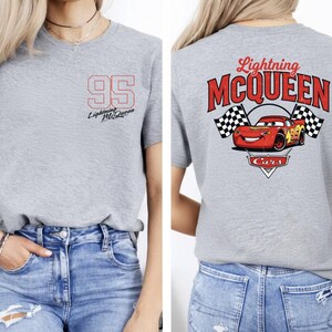 Puede incluir: Camiseta gris con el n&uacute;mero "95" y "Lightning McQueen" en la parte delantera. La parte trasera de la camiseta muestra un gr&aacute;fico de Rayo McQueen con banderas a cuadros y el texto "Lightning McQueen Cars".
