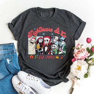Puede incluir: Una camiseta gris oscuro con un estampado gr&aacute;fico colorido de personajes de la pel&iacute;cula "Pesadilla antes de Navidad". El gr&aacute;fico incluye el texto "Nightmare & Co. Est. 1993".