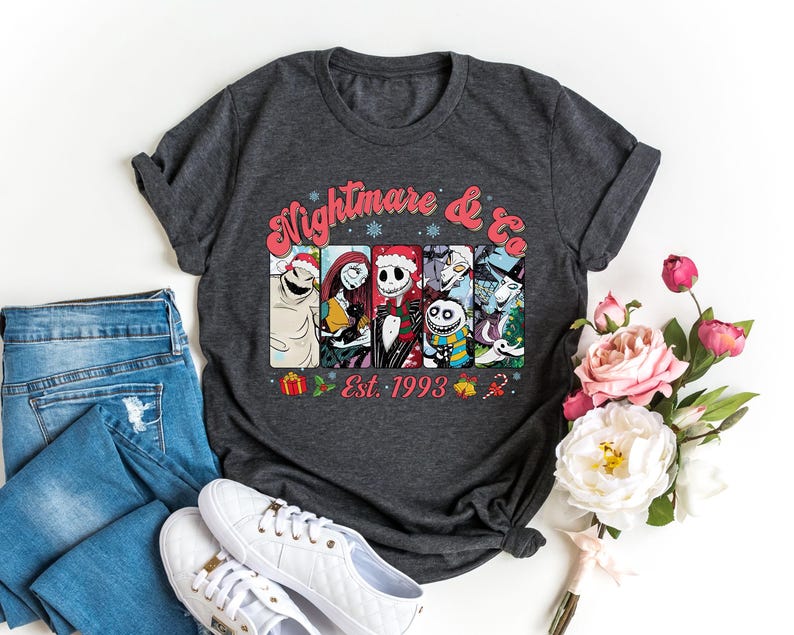 Puede incluir: Una camiseta gris oscuro con un estampado gr&aacute;fico colorido de personajes de la pel&iacute;cula "Pesadilla antes de Navidad". El gr&aacute;fico incluye el texto "Nightmare & Co. Est. 1993".