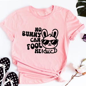 K&ouml;nnte beinhalten: Rosa T-Shirt mit einer schwarzen Grafik eines Kaninchens mit Sonnenbrille und dem Text "No bunny can fool me!"