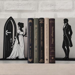 May include: A set of black metal bookends featuring silhouettes of a woman holding a candle by a doorway and a man in a tailcoat, flanking five copies of the book Northanger Abbey by Jane Austen with varying spine colours and gold lettering.