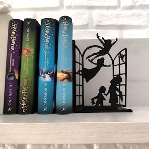 May include: A black metal bookend featuring a silhouette of figures in a window, with four "Harry Potter" books in a row. The books have colorful covers and the titles "Philosopher's Stone", "Chamber of Secrets", "Prisoner of Azkaban", and "Goblet of Fire".