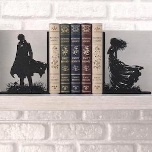 Puede incluir: Juego de sujetalibros con temática literaria. Los sujetalibros de metal negro presentan siluetas de figuras y sostienen una fila de libros "Cumbres Borrascosas" de Emily Bronte. Los libros tienen lomos de varios colores.
