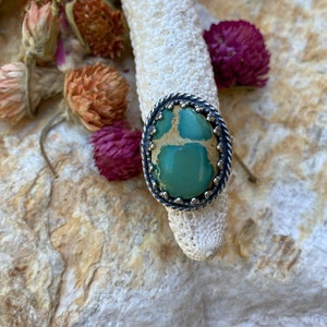 May include: A silver ring with a green and brown oval gemstone set in a beaded bezel.