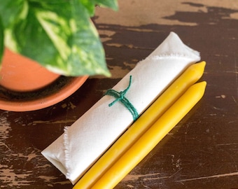 May include: Two yellow beeswax candles wrapped in a white cloth with a green string tied around them.