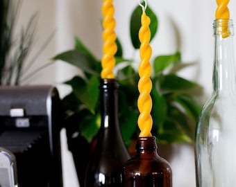 May include: Three yellow twisted candles in glass bottles. The bottles are clear, brown, and green. The candles are of varying sizes.