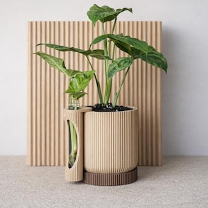 Puede incluir: Una moderna maceta beige con un diseño acanalado, que contiene una exuberante planta verde. La maceta incluye un compartimento lateral para plantas adicionales. Se asienta sobre una base circular marrón, con un fondo beige claro.