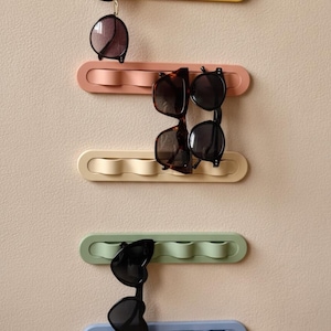 Peut inclure: Un organisateur mural pour lunettes de soleil en jaune, rose, crème, vert et bleu. Chaque organisateur peut contenir plusieurs paires de lunettes de soleil. Les lunettes de soleil sont noires et marron.