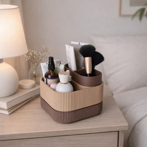 Op de afbeelding: Een tweekleurige beige en bruine cosmetica-organizer met een geribbeld ontwerp. De organizer bevat diverse schoonheidsproducten, waaronder borstels, flesjes en tubes. De organizer staat op een houten oppervlak naast een lamp.