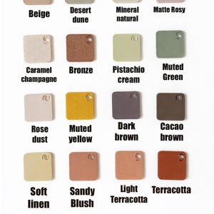 May include: Sixteen square colour swatches are displayed, showcasing a range of hues such as beige, desert dune, and matte rosy. Each swatch has a small hole and is labelled with its colour name in a sans-serif font. The colours vary from light to dark.