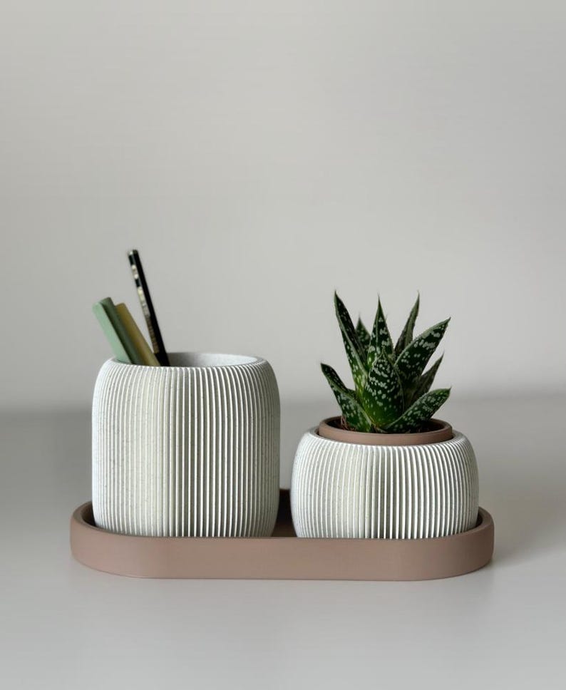 May include: A white, ribbed desk organiser set with a small succulent plant. The set includes a pencil holder with pencils and a small planter, both on a matching tray. The set is made of a light-coloured material.